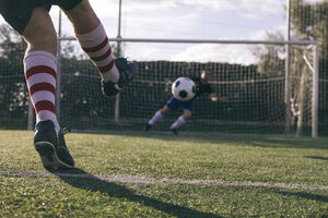 Beine eines Fußballspielers, der einen Ball vor ein Tor mit einem Torwart schießt - ABZF000448