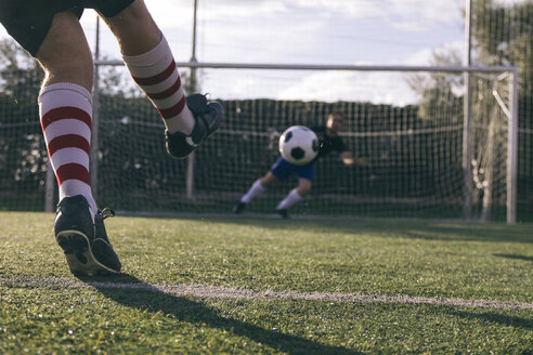 Legs of a footnball player kicking a ball in front of a goal with a goalkeeper - ABZF000448