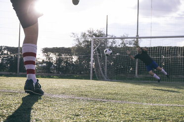 Beine eines Fußballspielers, der einen Ball vor ein Tor mit einem Torwart schießt - ABZF000450