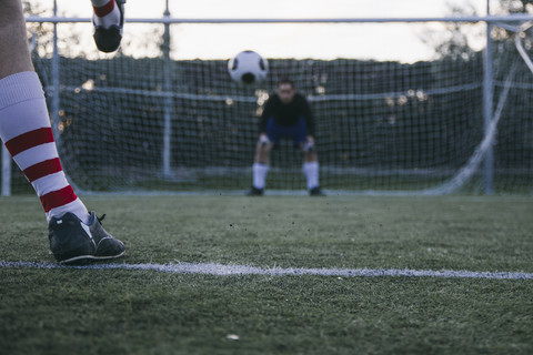 Beine eines Fußballspielers, der einen Ball vor ein Tor mit einem Torwart schießt, lizenzfreies Stockfoto