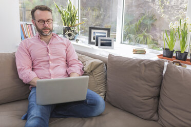 Älterer Mann sitzt auf der Couch und benutzt einen Laptop - BOYF000339