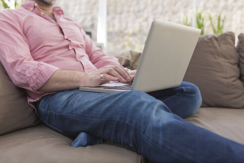Älterer Mann sitzt auf der Couch und benutzt einen Laptop - BOYF000340