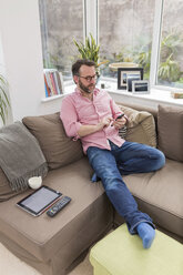 Mature man sitting on couch using smart phone - BOYF000344