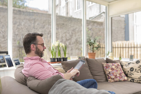 Älterer Mann sitzt auf der Couch und benutzt ein digitales Tablet - BOYF000349