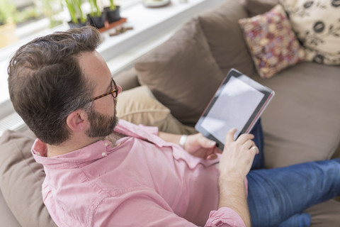Älterer Mann sitzt auf der Couch und benutzt ein digitales Tablet, lizenzfreies Stockfoto