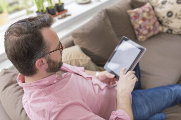 Älterer Mann sitzt auf der Couch und benutzt ein digitales Tablet - BOYF000350