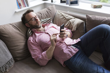 Mature mna lying on couch checking messages on smart phone - BOYF000352