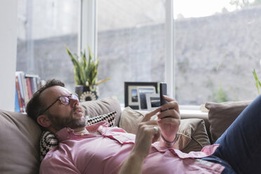 Reife Frau, die auf der Couch liegt und Nachrichten auf dem Smartphone überprüft - BOYF000354