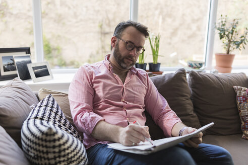 Älterer Mann sitzt auf der Couch und markiert Anzeigen in der Zeitung - BOYF000358