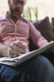 Älterer Mann sitzt auf der Couch und markiert Anzeigen in der Zeitung - BOYF000359