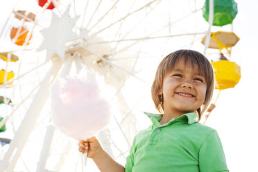 Portrait of happy little boy with cotton candy in front of big wheel - VABF000480