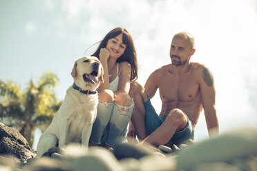 Paar sitzt mit seinem Hund am steinigen Strand - SIPF000419