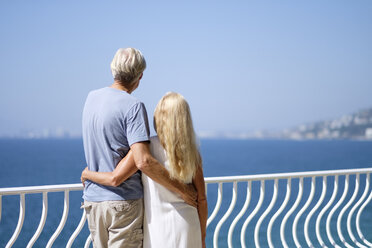 Senior couple looking at view on balcony by the sea - ABAF002007
