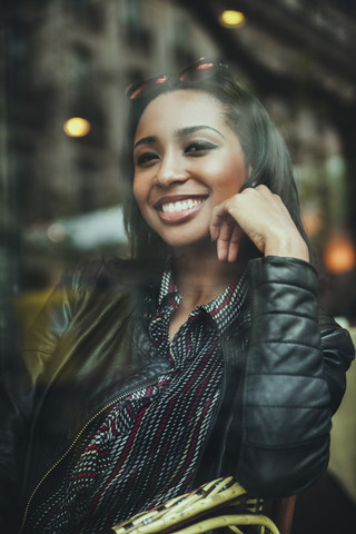 Porträt einer lächelnden jungen Frau, die hinter der Fensterscheibe eines Cafés sitzt, lizenzfreies Stockfoto