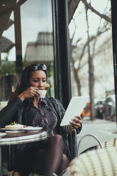 Porträt einer jungen Frau, die in einem Café sitzt, auf ein digitales Tablet schaut und Kaffee trinkt - ZEDF000093
