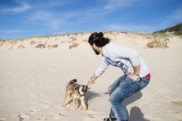 Man playing with his mongrel on the beach - RAEF001140