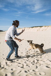 Mann spielt mit seinem Mischling am Strand - RAEF001141