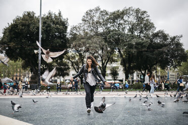 Spain, Barcelona, playful young woman with pigeons on a square - JRFF000619