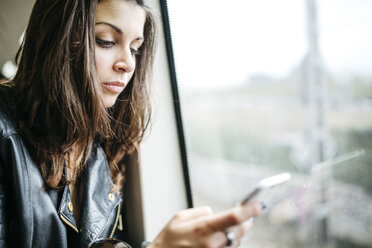 Junge Frau im Zug schaut auf ihr Handy - JRFF000630