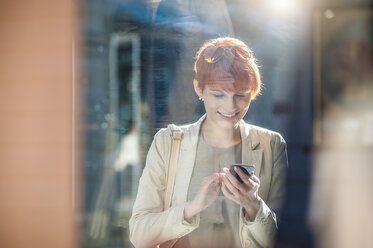 Lächelnde junge Frau, die am Schaufenster ein Mobiltelefon benutzt - DIGF000396