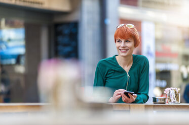 Smiling young woman using cell phone at outdoor cafe - DIGF000410