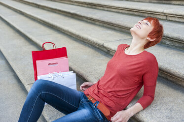 Lächelnde junge Frau entspannt sich auf einer Treppe mit Einkaufstüten neben sich - DIGF000421