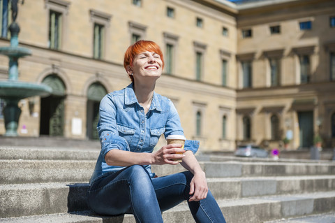 Junge Frau entspannt sich auf einer Treppe mit Kaffee zum Mitnehmen, lizenzfreies Stockfoto