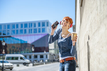 Happy young woman with coffee to go listening to music - DIGF000448