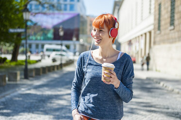 Lächelnde junge Frau mit Kaffee zum Mitnehmen, die Musik hört - DIGF000449