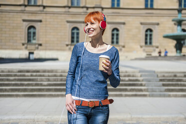 Lächelnde junge Frau mit Kaffee zum Mitnehmen, die Musik hört - DIGF000451