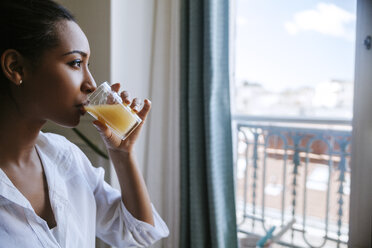 Junge Frau trinkt ein Glas Saft und schaut durch ein Fenster - ZEDF000095
