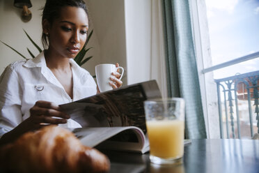 Portrait of young woman reading magazine at breakfast table - ZEDF000099