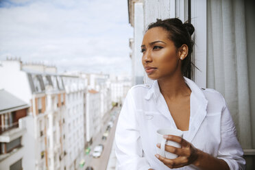 France, Paris, portrait of young woman with cup of coffee looking at distance - ZEDF000105