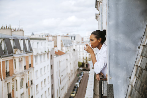 Frankreich, Paris, junge Frau mit Tasse Kaffee, die sich aus dem Fenster lehnt, lizenzfreies Stockfoto