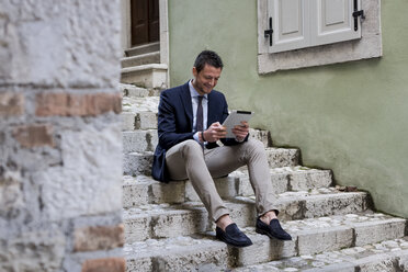 Geschäftsmann sitzt auf einer Steintreppe und benutzt ein digitales Tablet - MAUF000537