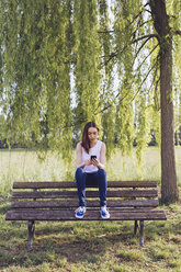 Junge Frau mit Telefon sitzt auf einer Bank im Park - GIOF000930