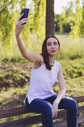 Woman taking a selfie while sitting a bench at the park - GIOF000932