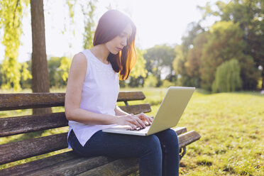 Frau lernt am Laptop, während sie auf einer Bank im Park sitzt - GIOF000935
