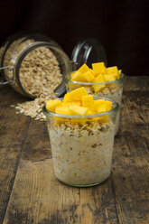 Zwei Gläser Overnight Oats mit gewürfelter Mango auf Holz - LVF004851