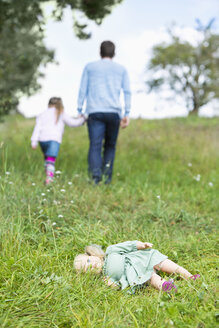 Puppe auf der Wiese liegend, während der Mann mit dem kleinen Mädchen weggeht - MAEF011553