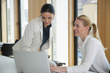 Zwei Geschäftsfrauen im Büro arbeiten gemeinsam an einem Laptop - CHAF001686