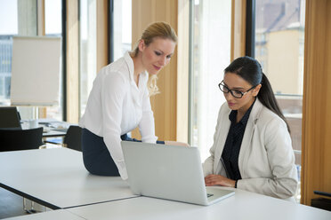 Zwei Geschäftsfrauen im Büro arbeiten gemeinsam an einem Laptop - CHAF001687