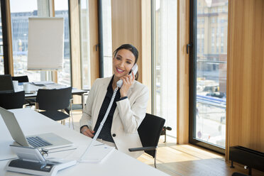 Smiling businesswoman at office desk on the phone - CHAF001690