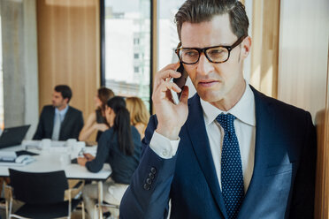 Geschäftsmann am Telefon mit Meeting im Hintergrund - CHAF001713