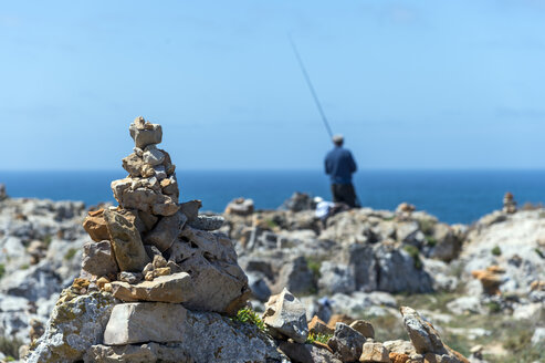 Portugal, Algarve, Sagres, Steinhaufen an der Küste, Angler im Hintergrund - FRF000418