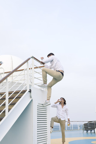 Zwei junge Männer tummeln sich auf einem Kreuzfahrtschiff und klettern auf die Reling, lizenzfreies Stockfoto