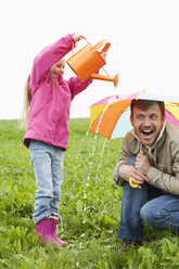 Vater mit Gießkanne und Tochter mit Regenschirm auf einer Wiese - MAEF011613