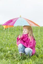 Junges Mädchen mit Regenschirm auf einer Wiese hockend, Regenwetter - MAEF011614