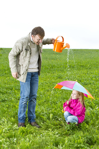 Vater mit Gießkanne und Tochter mit Regenschirm auf einer Wiese, lizenzfreies Stockfoto