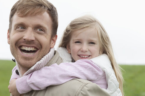 Glücklicher Vater trägt Tochter huckepack im Freien - MAEF011622
